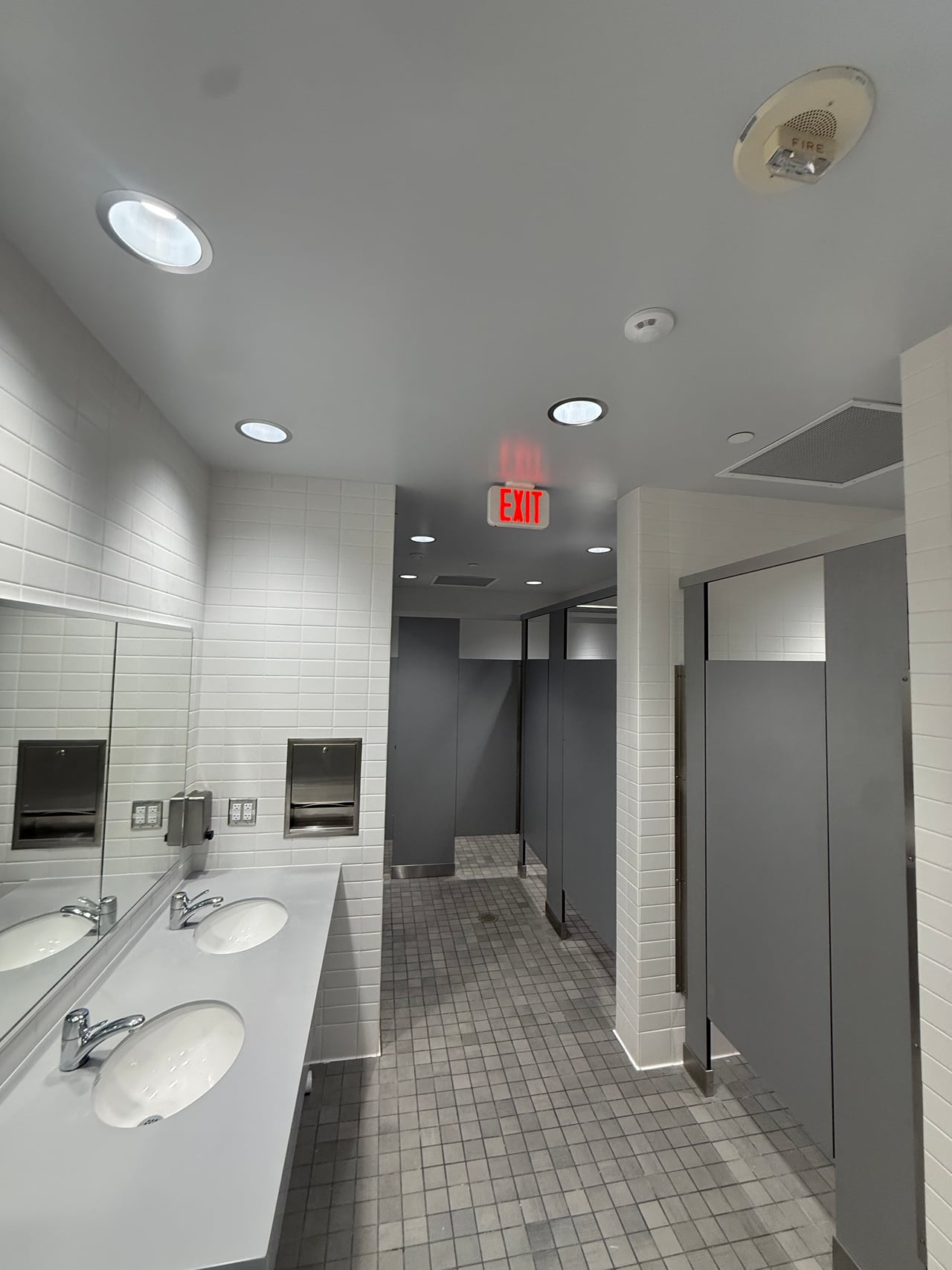 Recessed ceiling lights and electrical outlets above sinks in the remodeled restroom