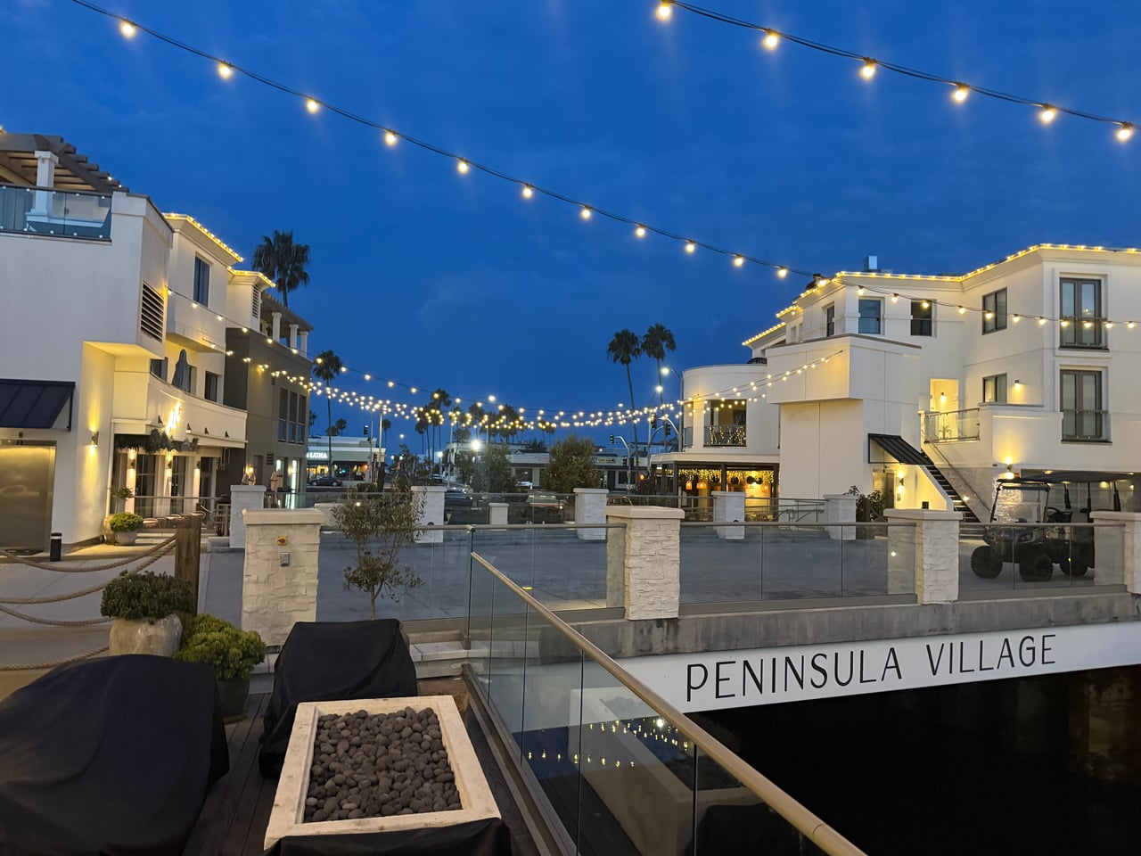 Illuminated courtyard and waterfront buildings at Peninsula Village in Newport Beach