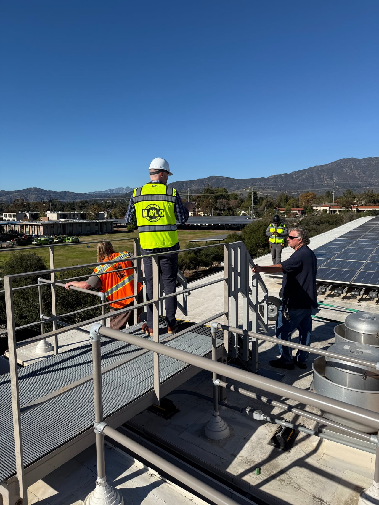 A Halo crew member and other team members beside a rooftop solar array