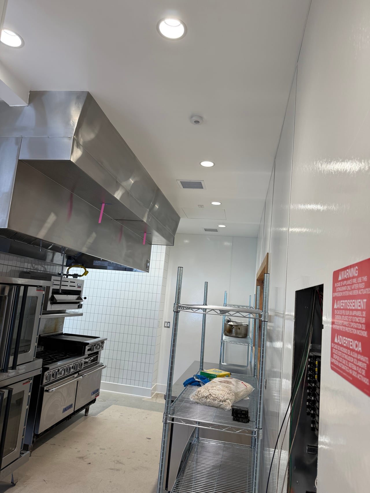 Commercial kitchen equipment beneath a hood with recessed ceiling lighting at Rye Goods